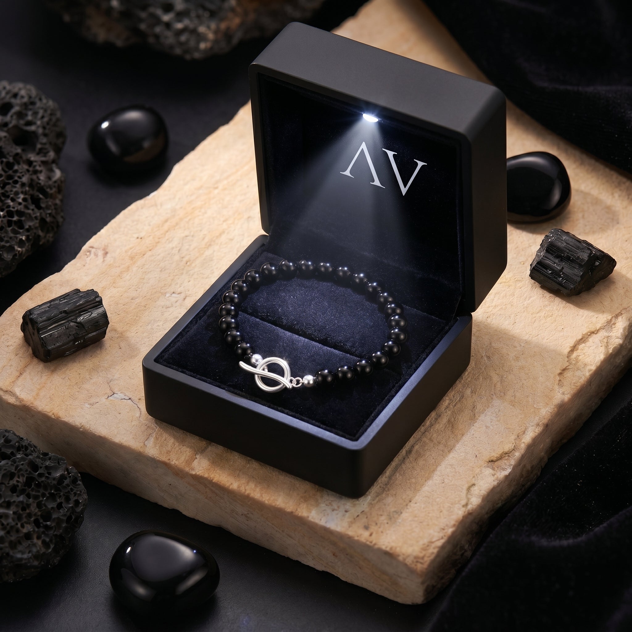 Black onyx bead bracelet with a silver clasp inside a premium LED-lit jewelry gift box on a stone surface.