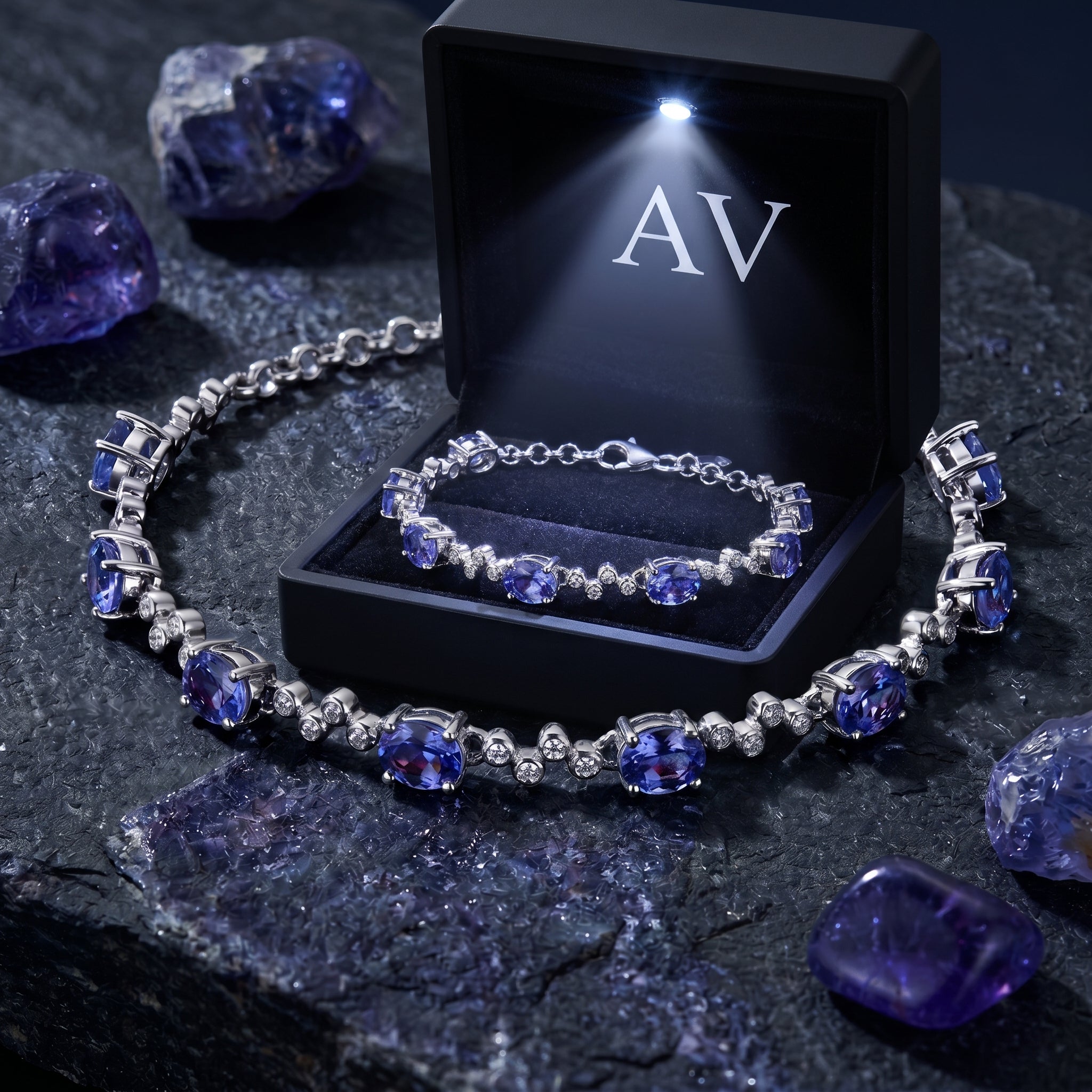 Natural tanzanite station bracelet presented in a black LED-lit jewelry gift box on a dark stone surface.