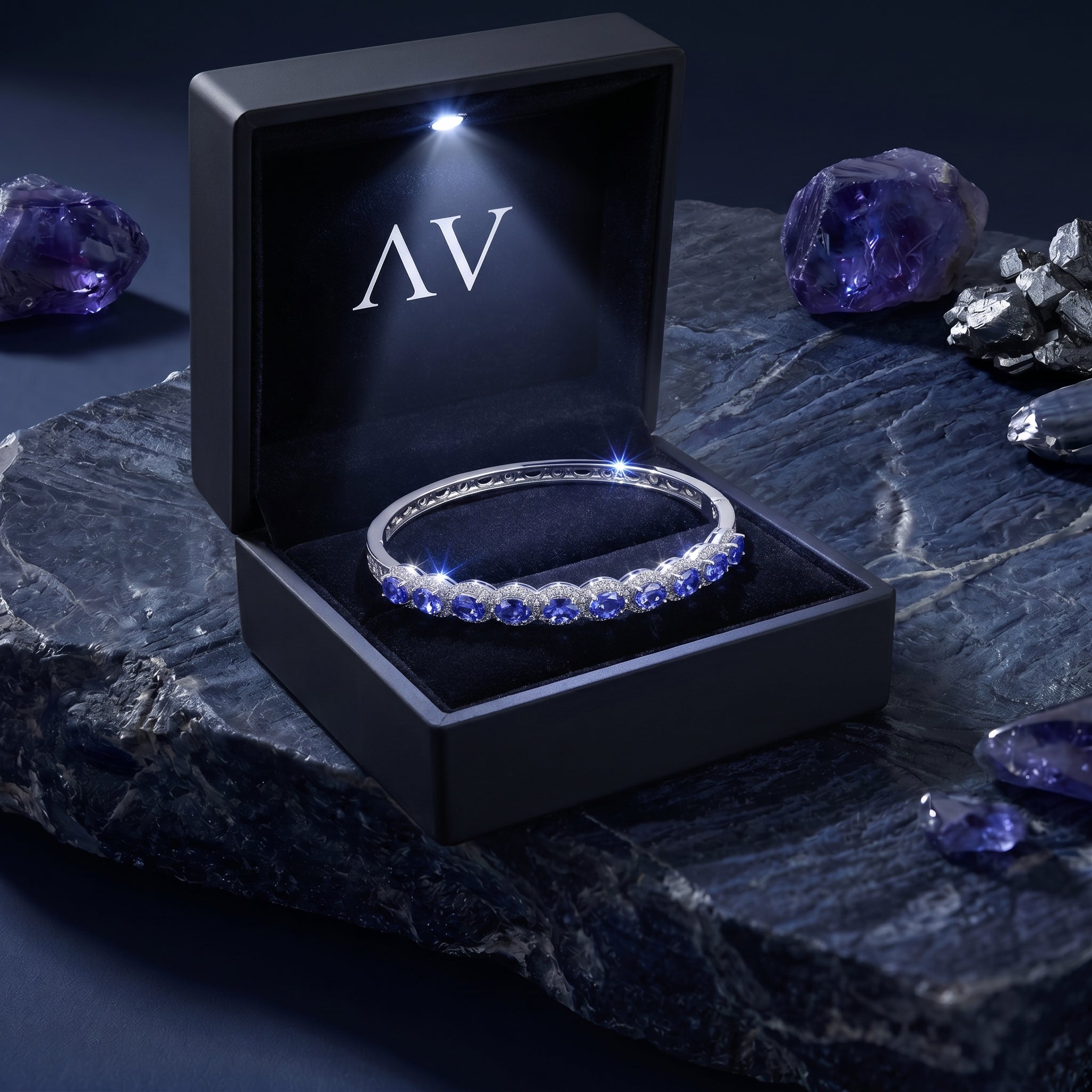 Natural tanzanite white gold bracelet presented in a black LED-lighted gift box on a dark stone base.
