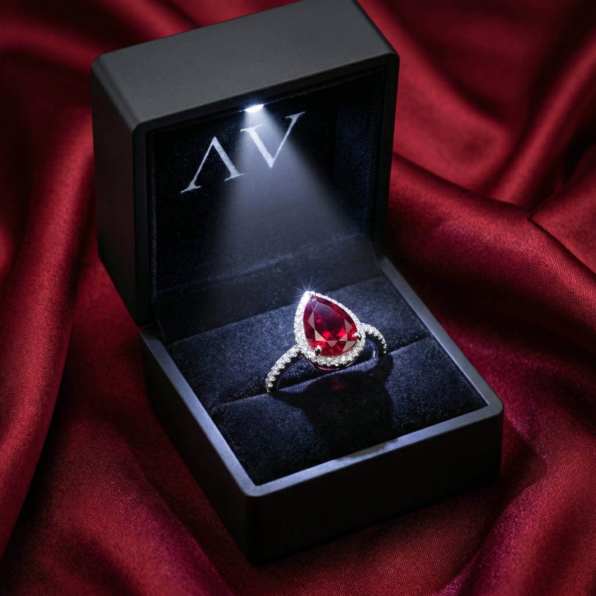 Pear-cut simulated ruby sterling silver ring in a black LED-lit jewelry box on red fabric.