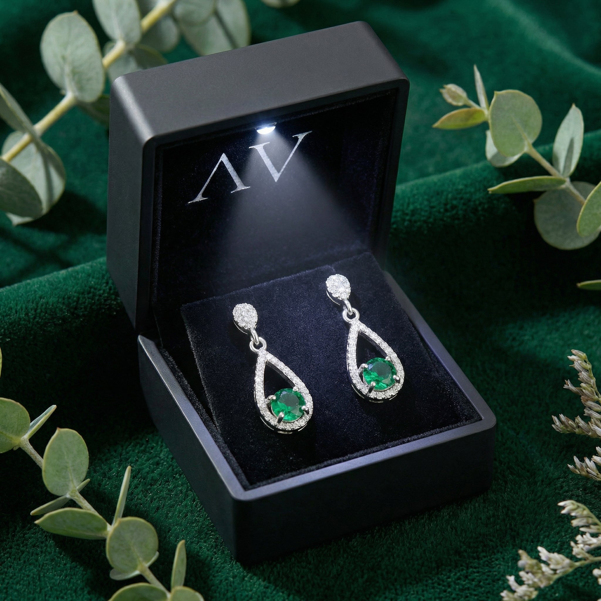 Sterling silver simulated emerald drop earrings presented in a black lighted jewelry gift box on green velvet.