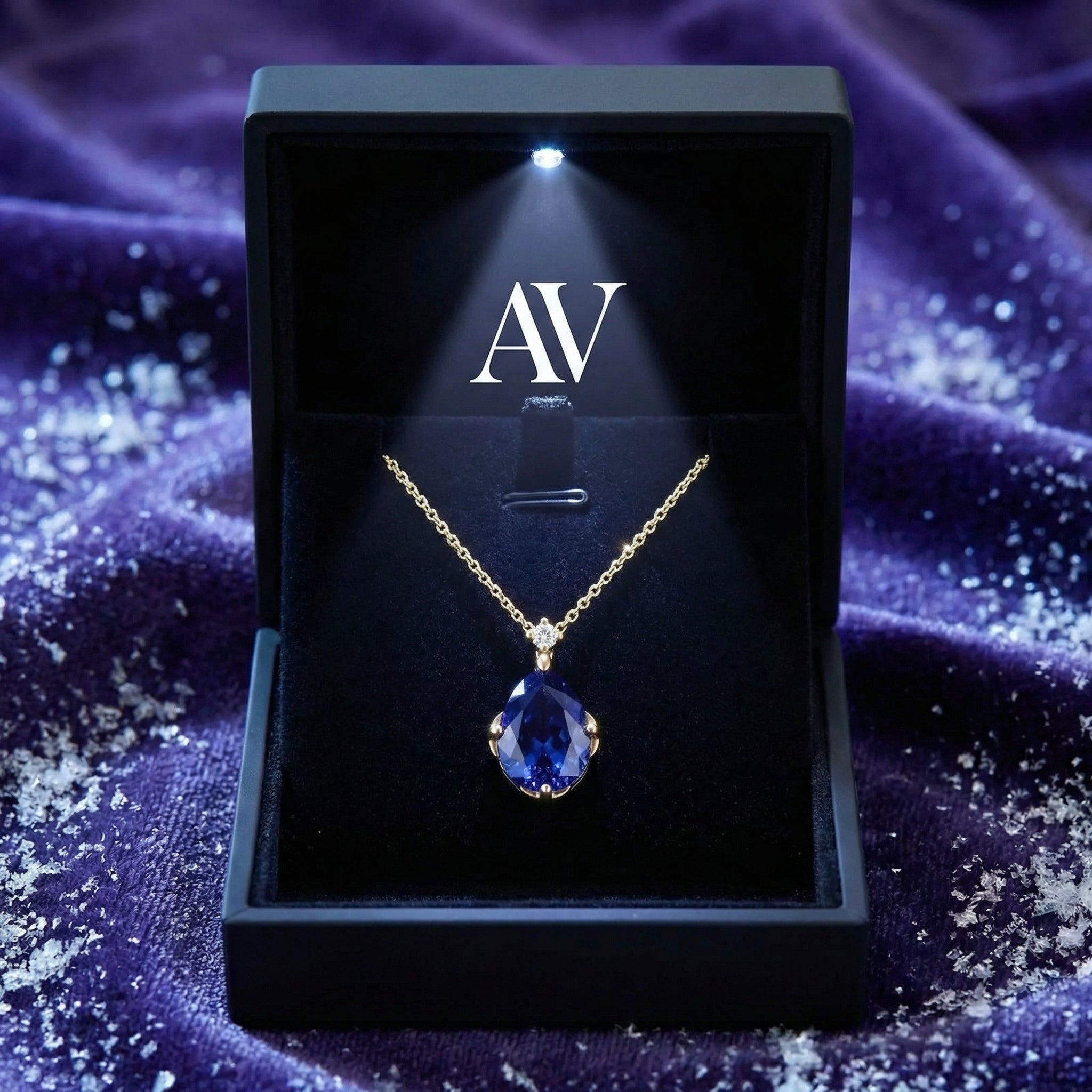 Gold teardrop simulated tanzanite necklace displayed in a black lighted jewelry box with AV branding.
