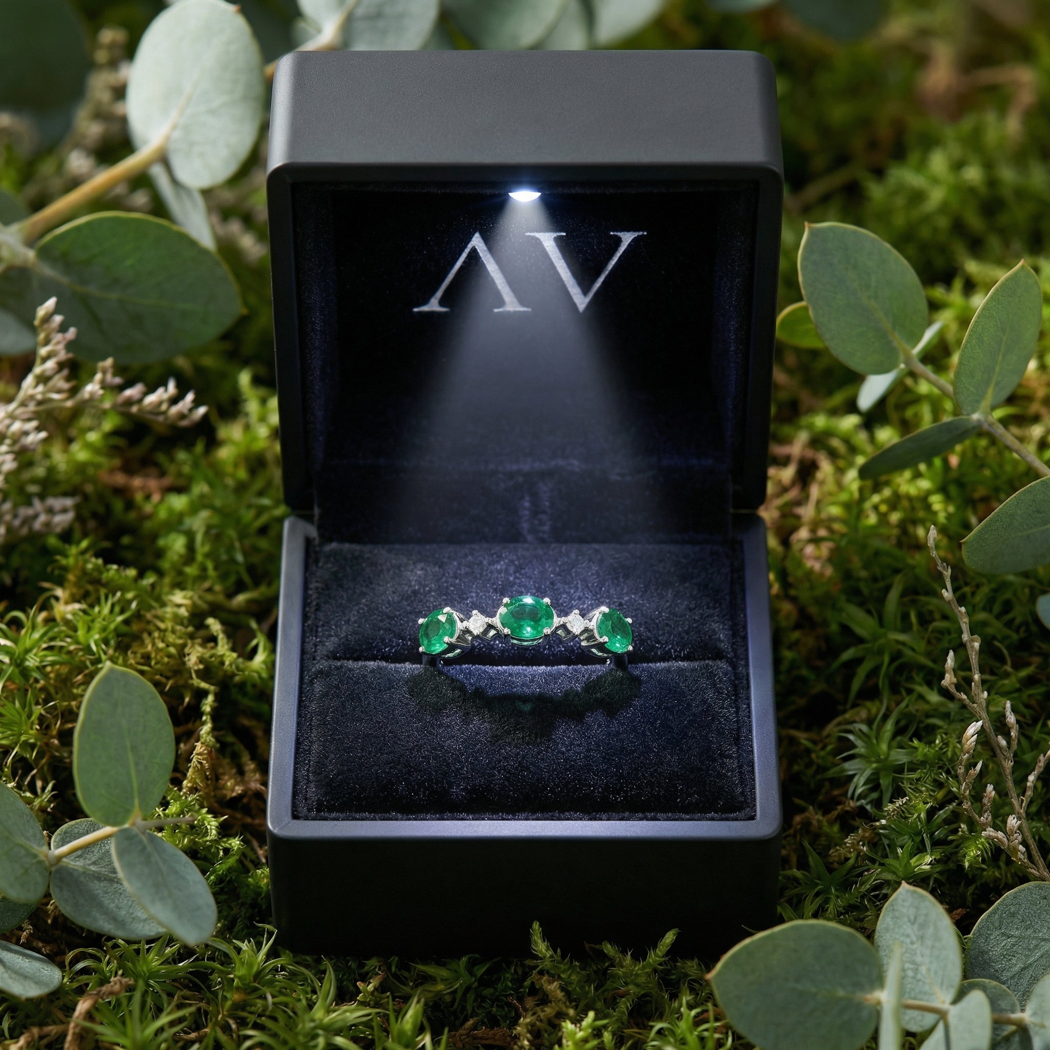 Sterling silver bypass ring with three oval simulated emeralds inside a black LED-lit jewelry box.