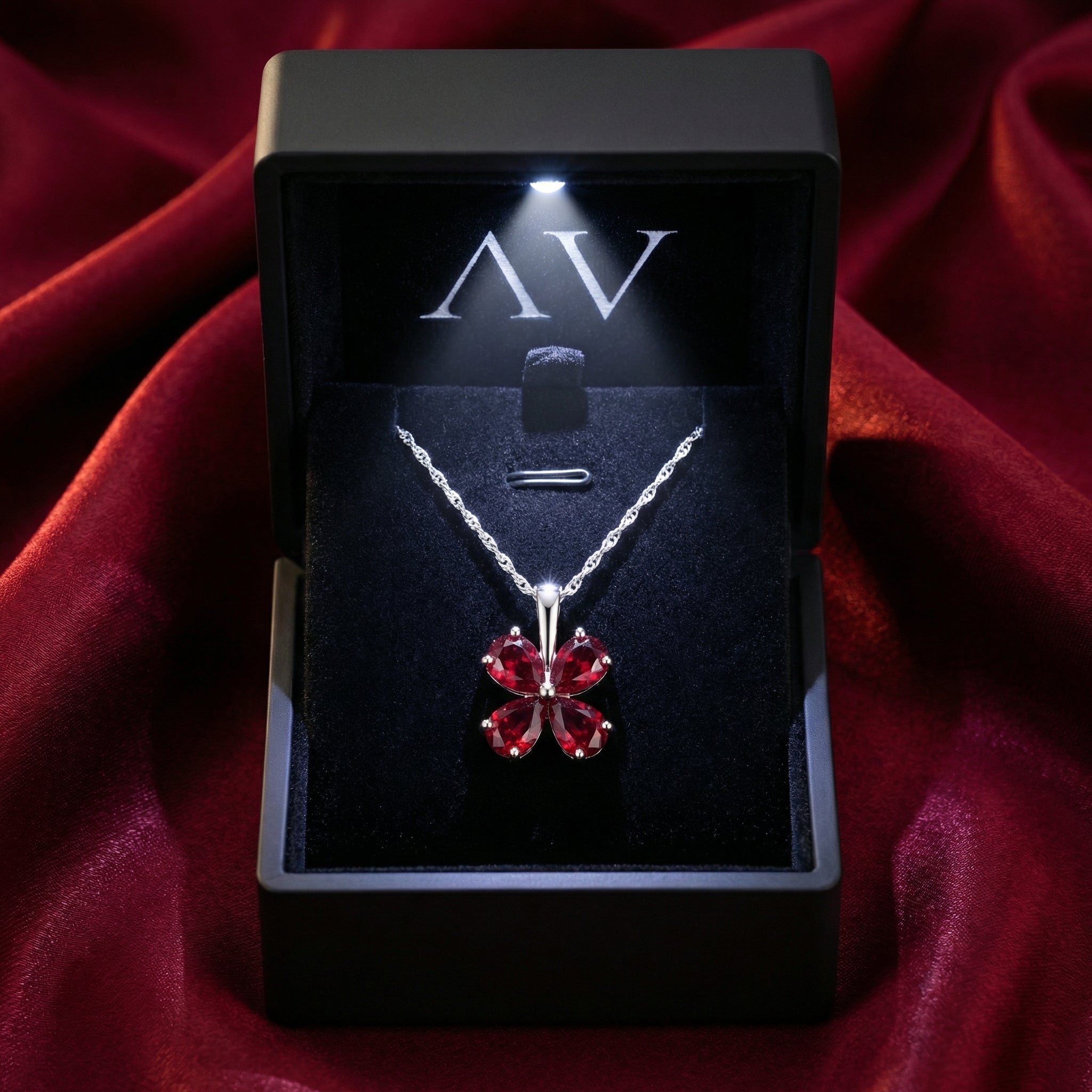 Simulated ruby blossom necklace in a black LED-lit jewelry gift box on a red silk background.