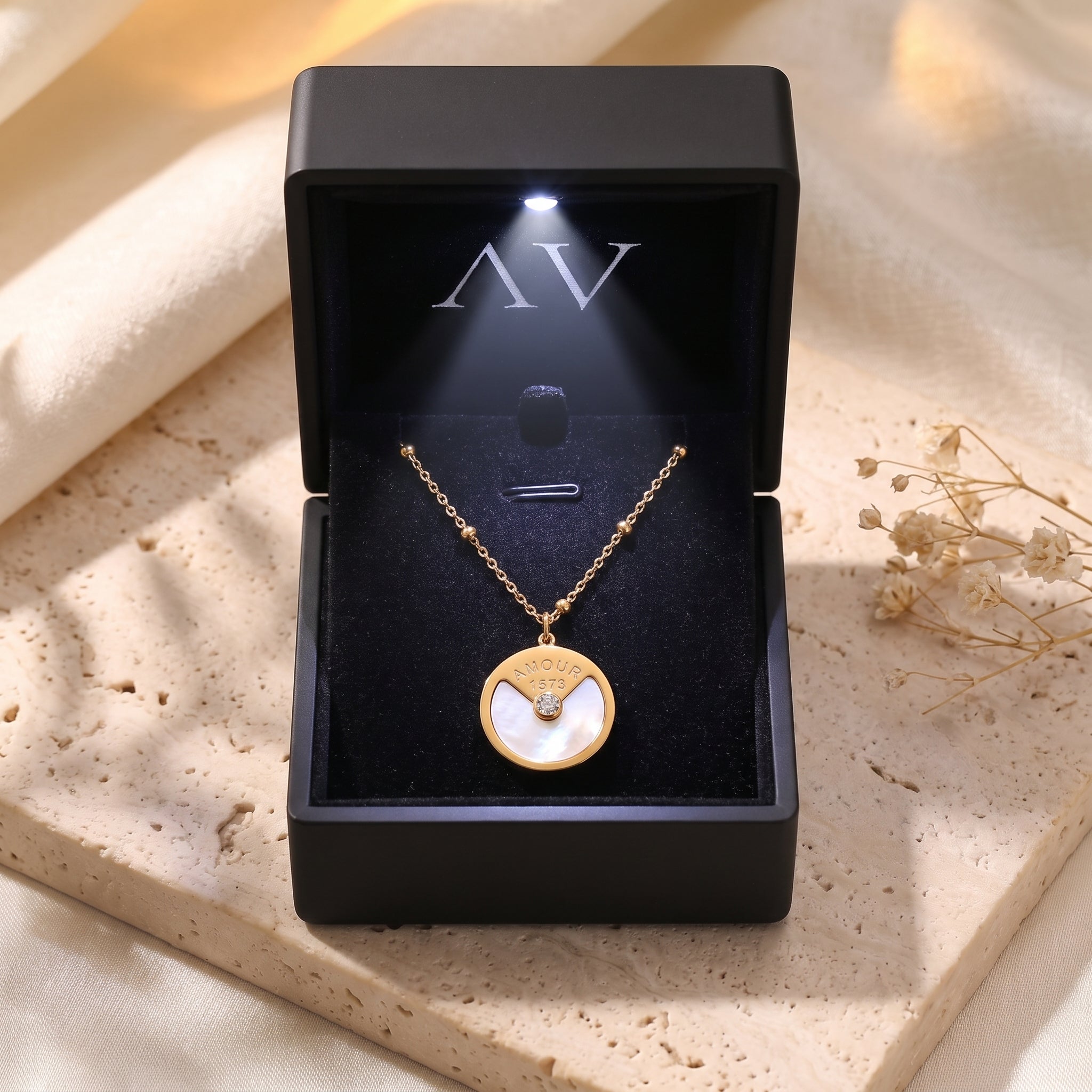 Gold pendant necklace inside a black LED-lit jewelry box on a stone surface.