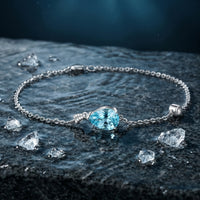 Pear-cut aquamarine platinum bracelet on a dark wet stone surface with water droplets and crystals.
