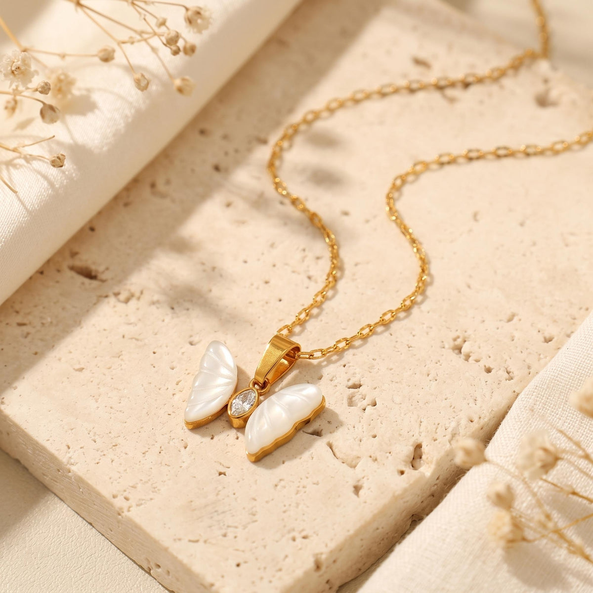 Mother-of-pearl butterfly pendant with gold-tone chain and clear stone center on a neutral stone slab.