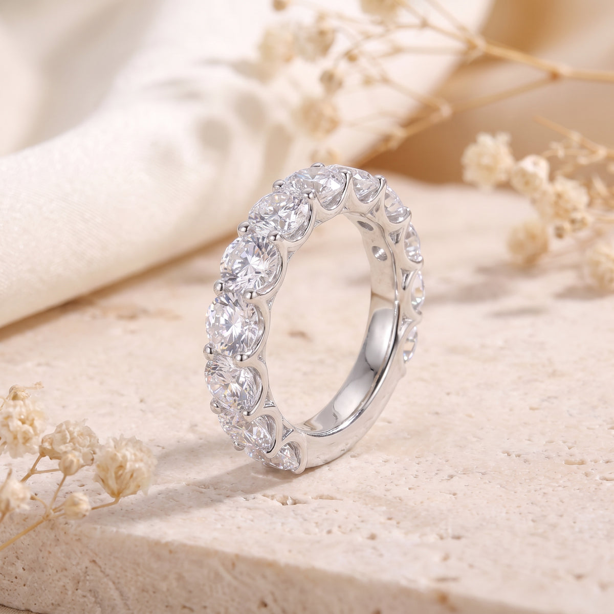 Angled close-up of a silver eternity ring with round clear stones in a scalloped shared-prong setting.