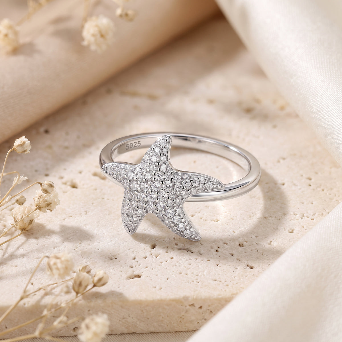 Close-up of a silver starfish ring with pave-set clear stones resting on a textured stone surface.