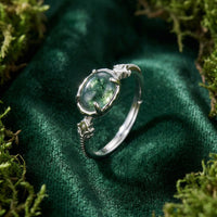 Oval natural moss agate ring in solid gold with leaf engravings on a green mossy background.