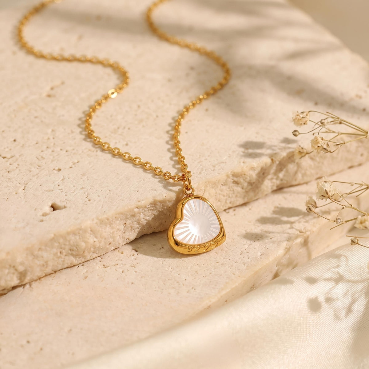 Gold-tone chain with a sunburst heart pendant, displayed on a textured stone block.