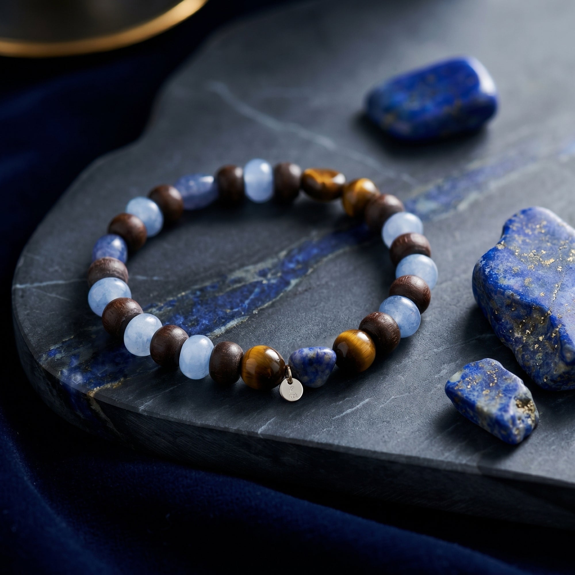 The Stargazer Natural Lapis Bracelet with round lapis and tiger's eye beads and gold plated charm on a stone slab.