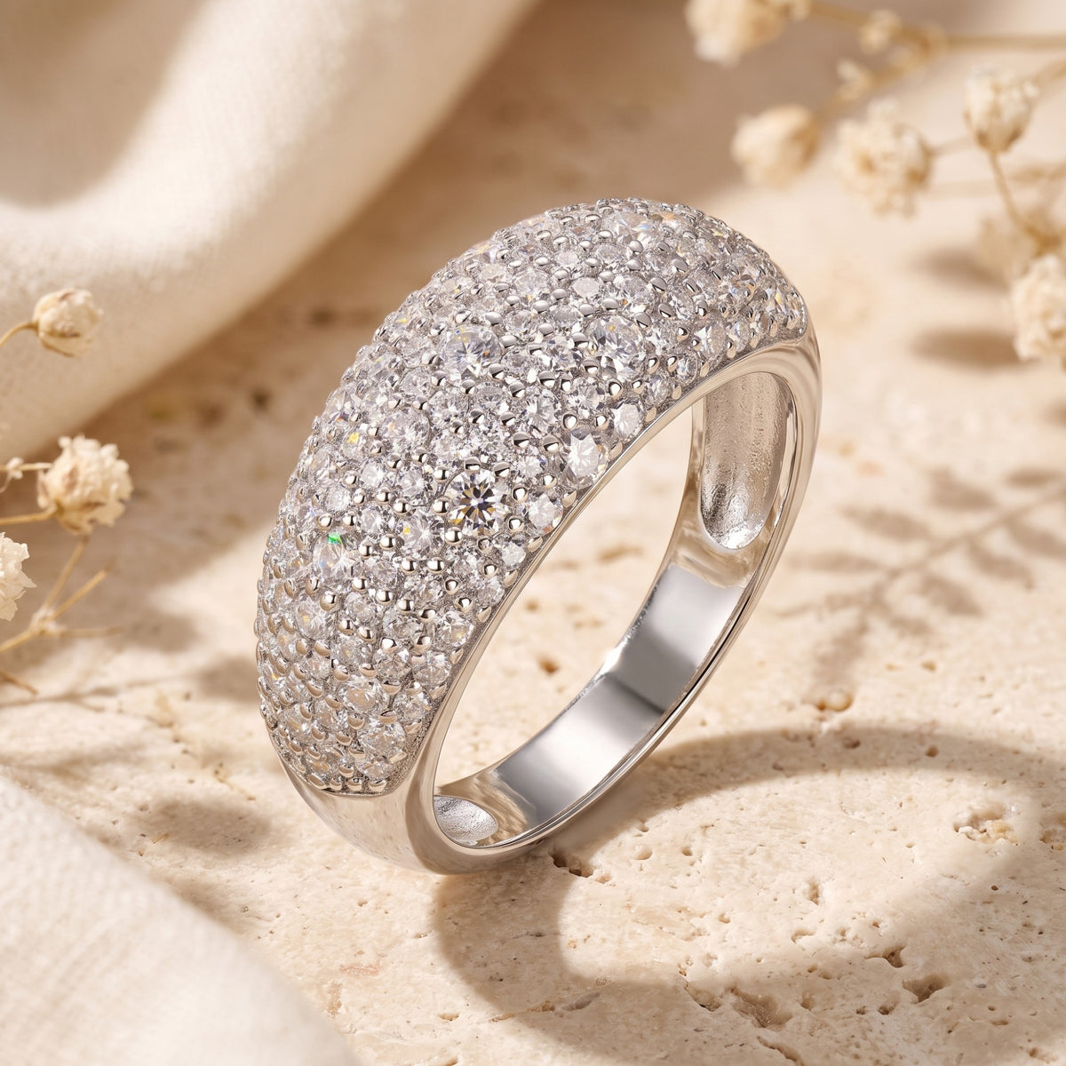 Solid white gold dome ring with pave-set cubic zirconia on a stone surface with dried flowers.