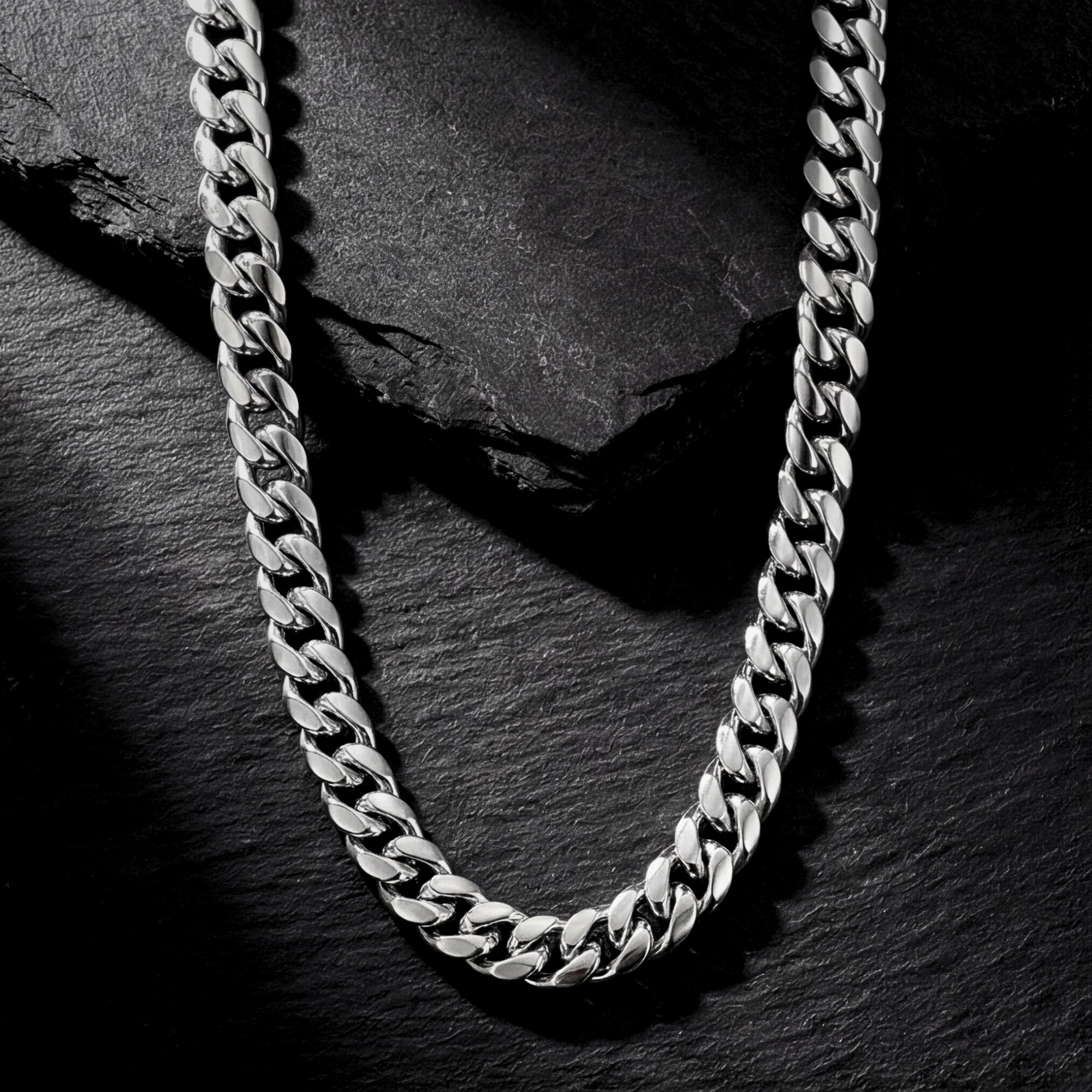 Silver 8mm stainless steel Cuban link chain laid on a dark textured slate background.