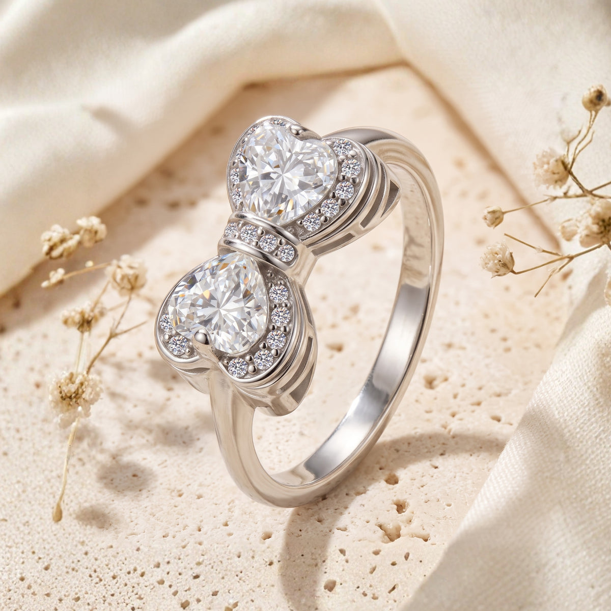 Close-up angled view of a silver bow ring with two halo-framed heart stones.