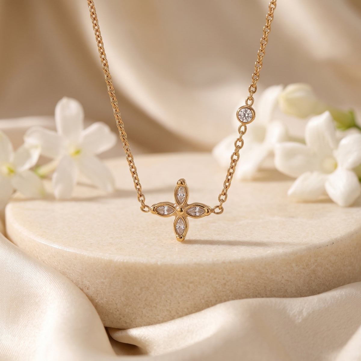 Front view of the gold-tone four-petal flower necklace hanging over a beige pedestal display.