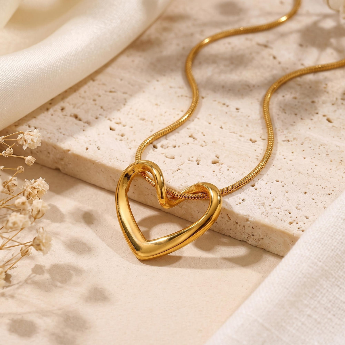 Gold-tone fluid open heart pendant on a snake chain, displayed close up on a textured stone slab.