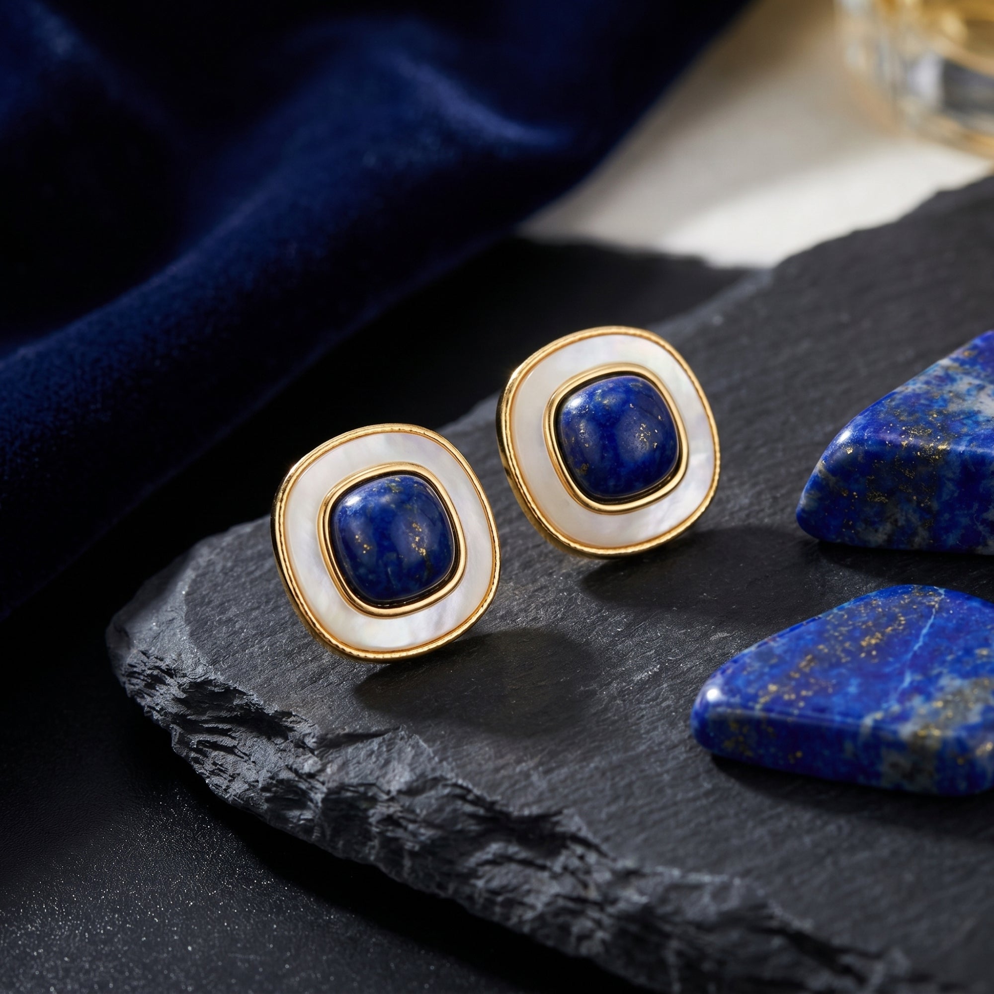 Gold-plated cushion-cut natural lapis lazuli earrings with white borders on a slate rock lifestyle background.