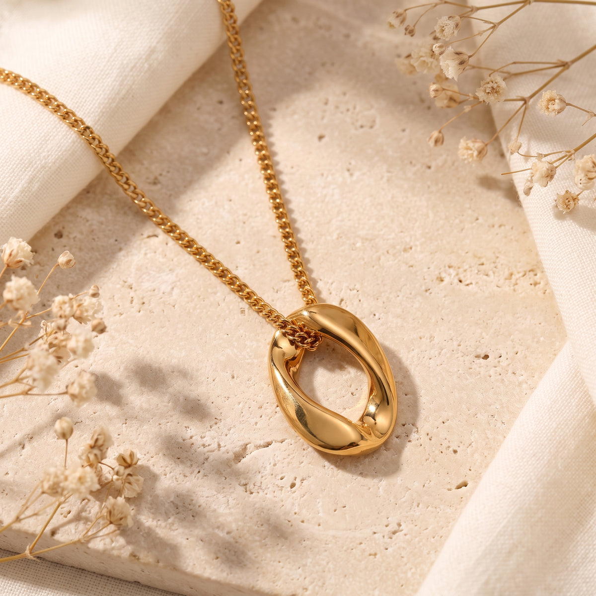 Gold-tone sculptural organic oval pendant necklace displayed flat on a beige stone surface.