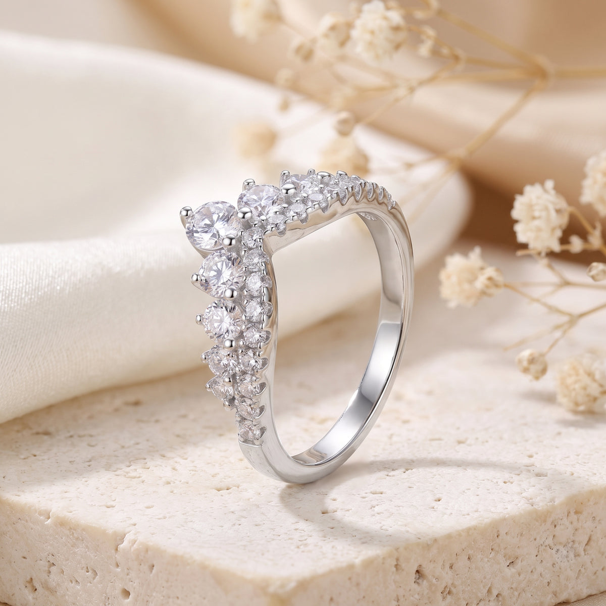 Silver chevron promise ring with round-cut cubic zirconia on a stone surface with dried flowers.