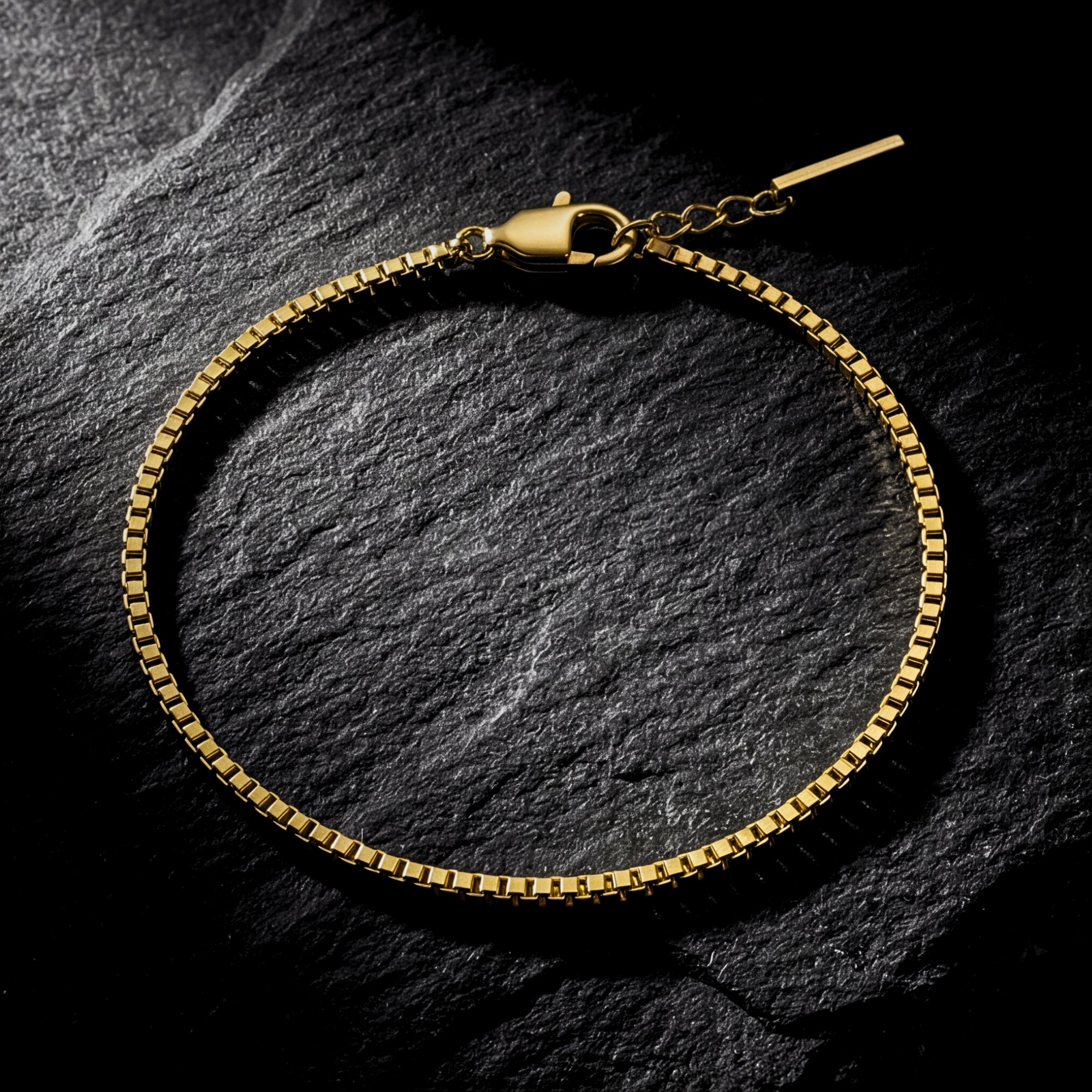 Gold stainless steel box chain bracelet for men displayed on a dark textured stone background.