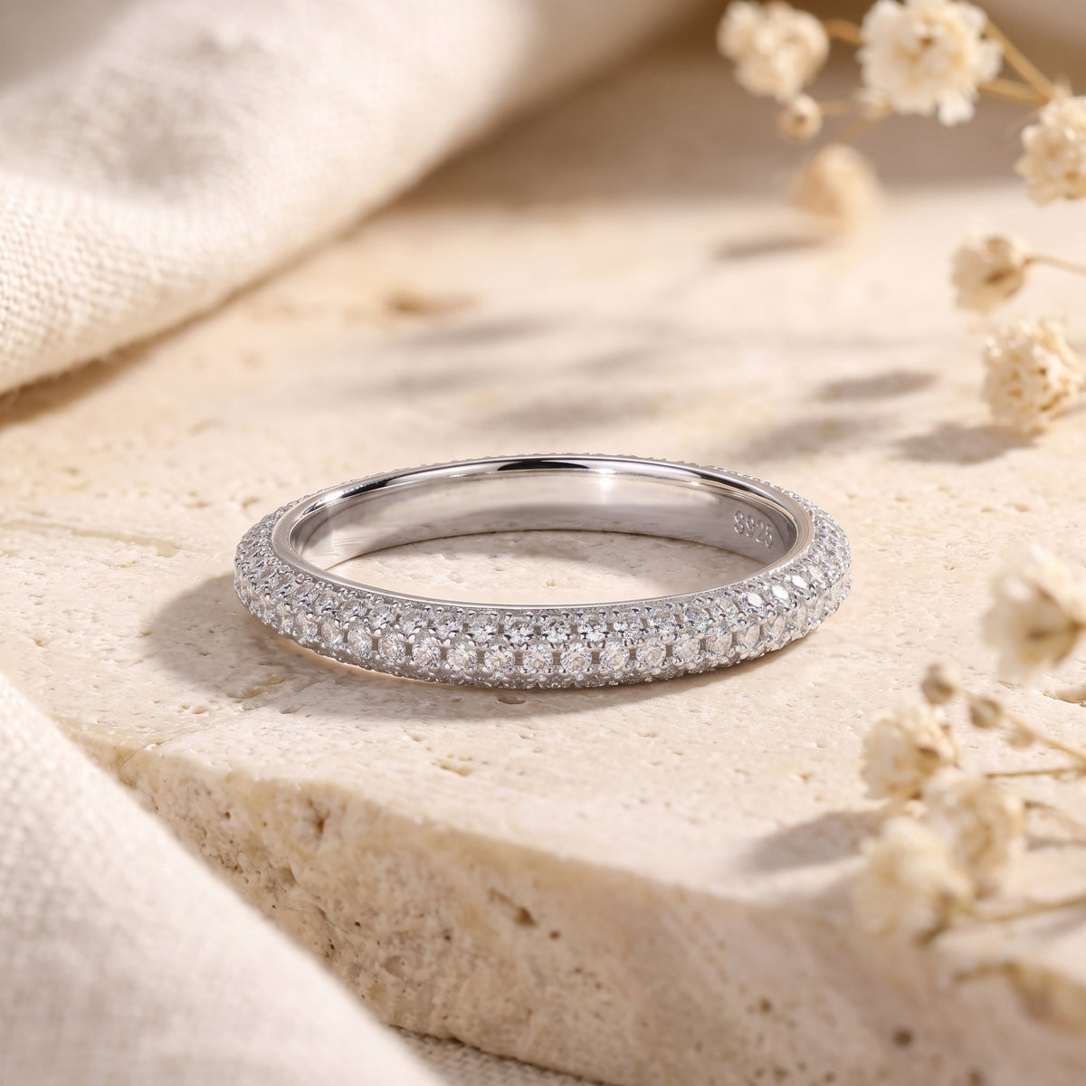 Silver multi-row pavé band ring resting flat on a beige travertine surface.