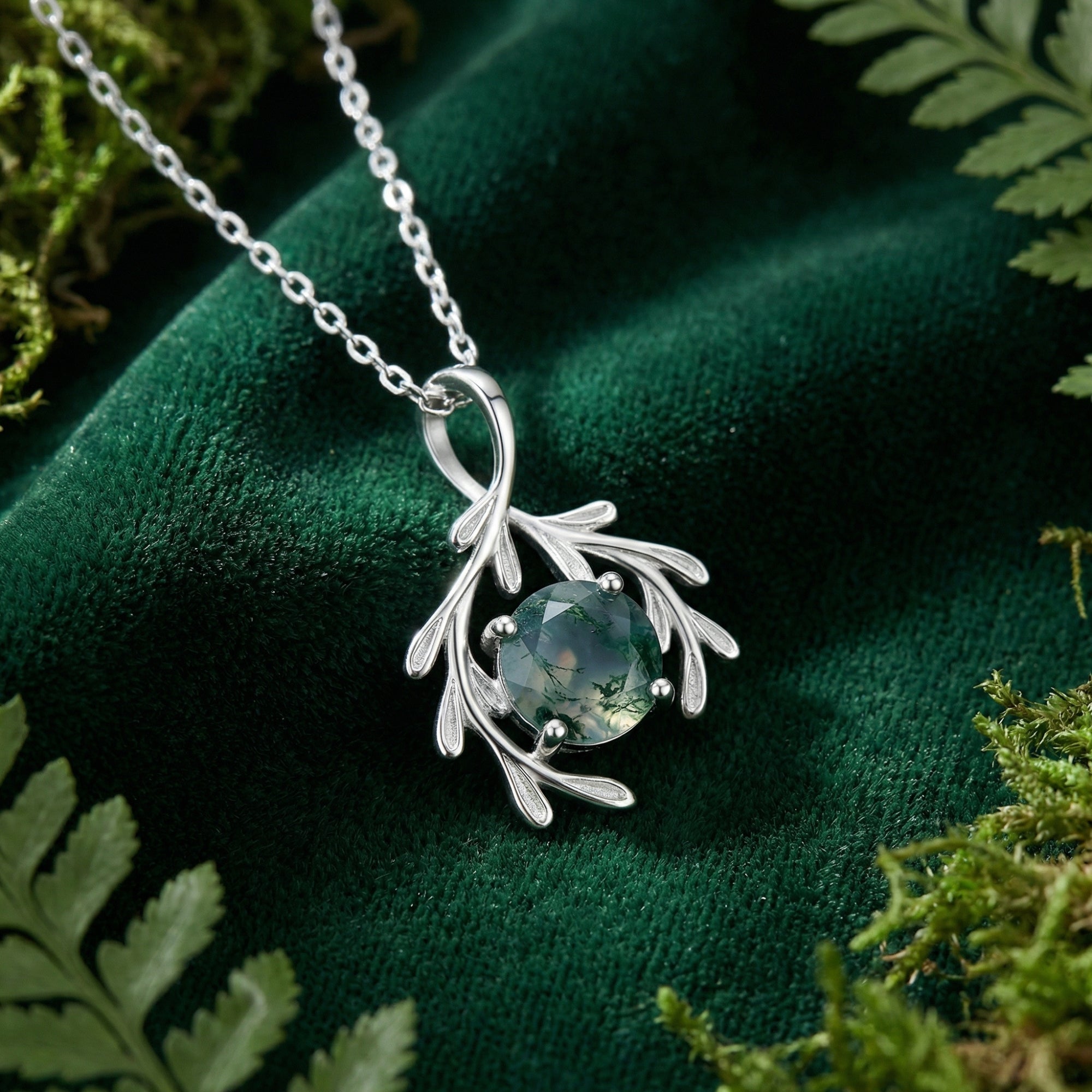 Detail of a round cut moss agate stone in a sterling silver branch pendant on green velvet.