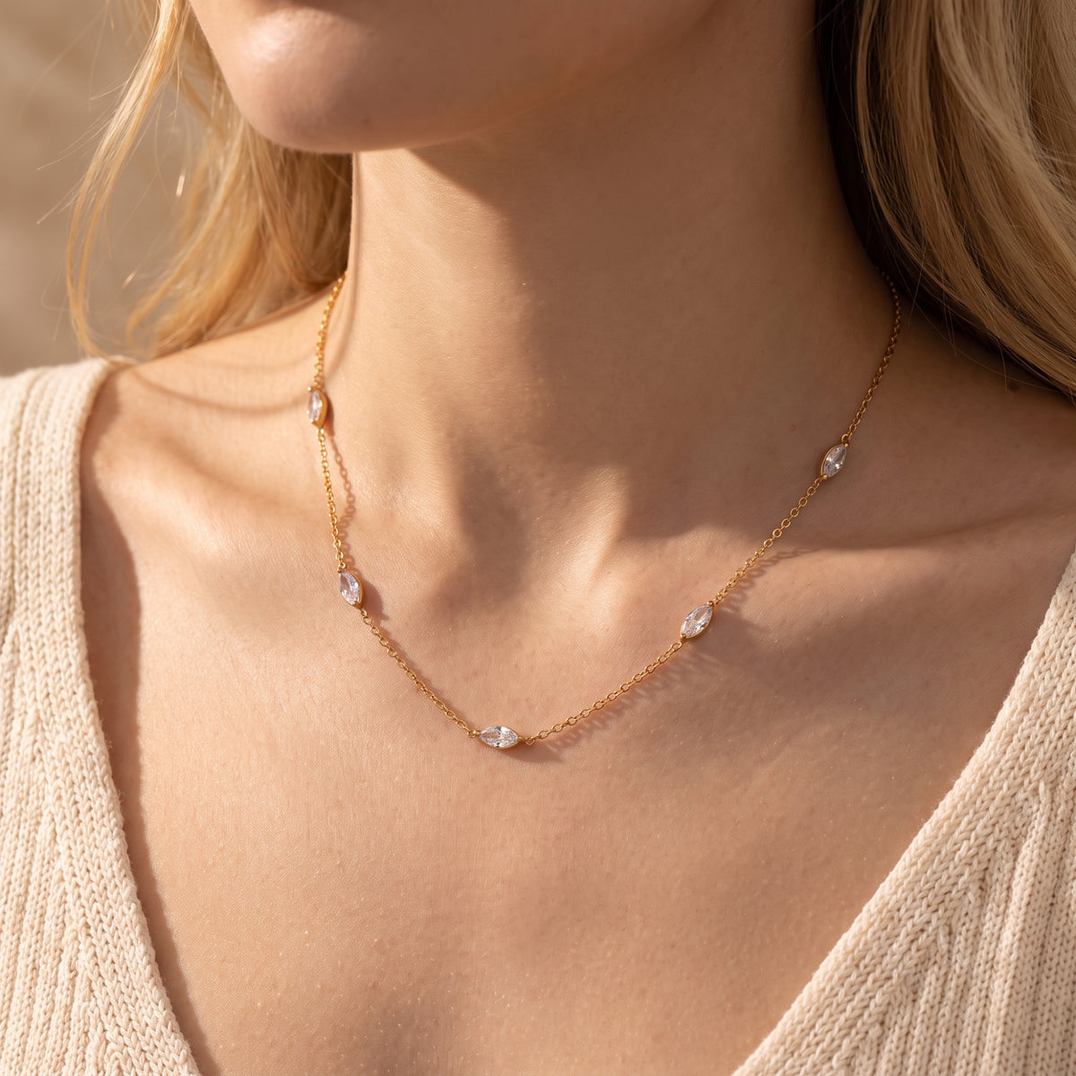 Model wearing the gold-tone station necklace with clear marquise-cut stones and a ribbed cream top.