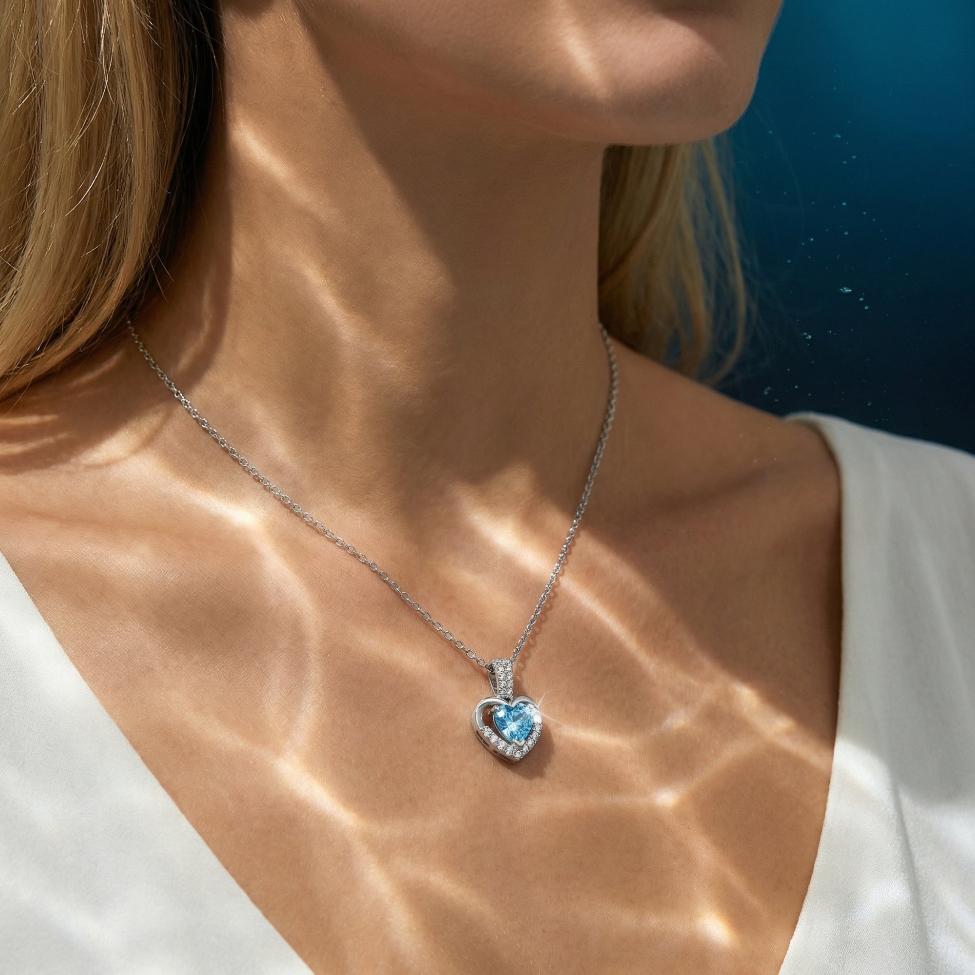 Heart-cut aquamarine platinum necklace worn by a model with shimmering water-like light patterns on her skin.