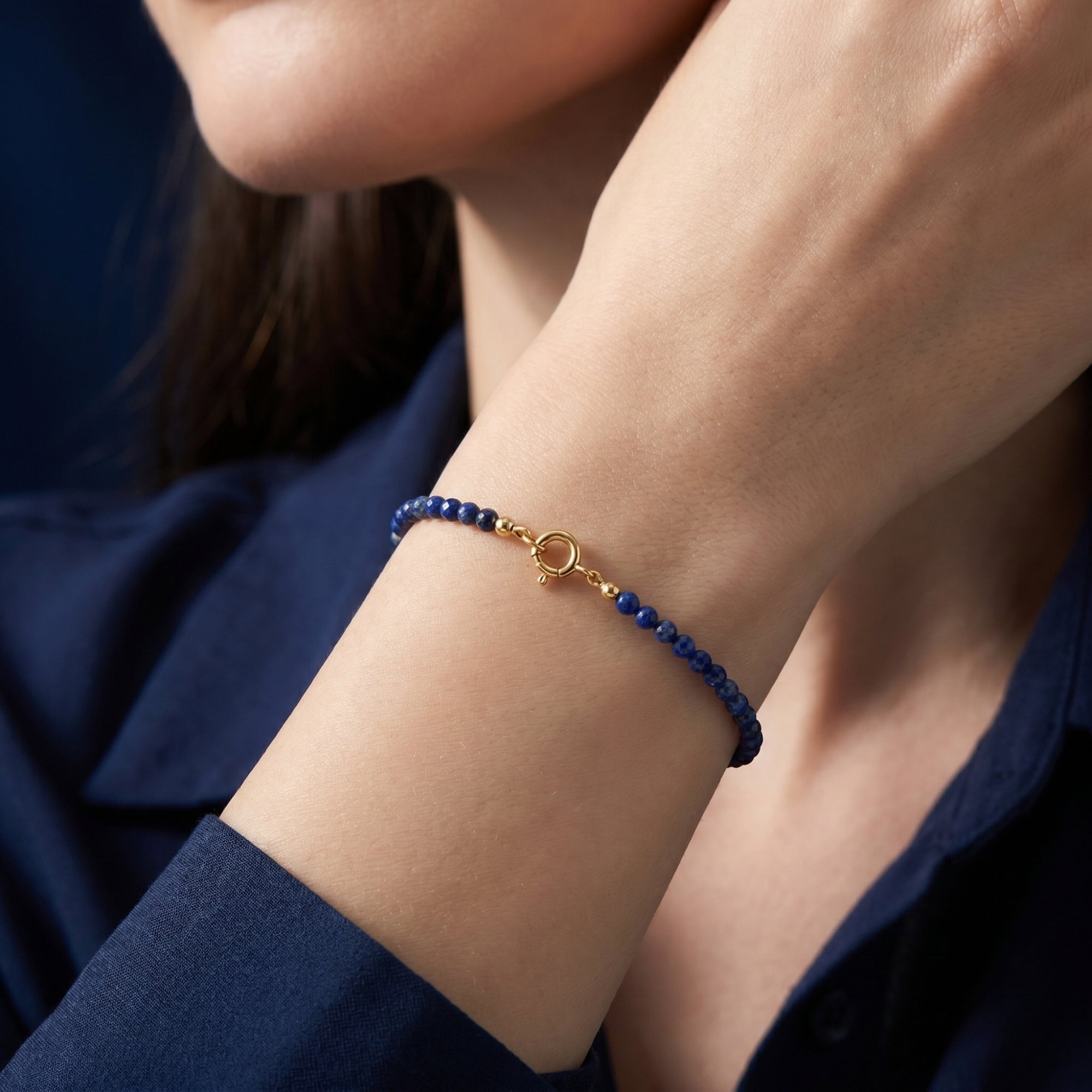 Faceted lapis lazuli bead bracelet with gold clasp worn on a woman's wrist.