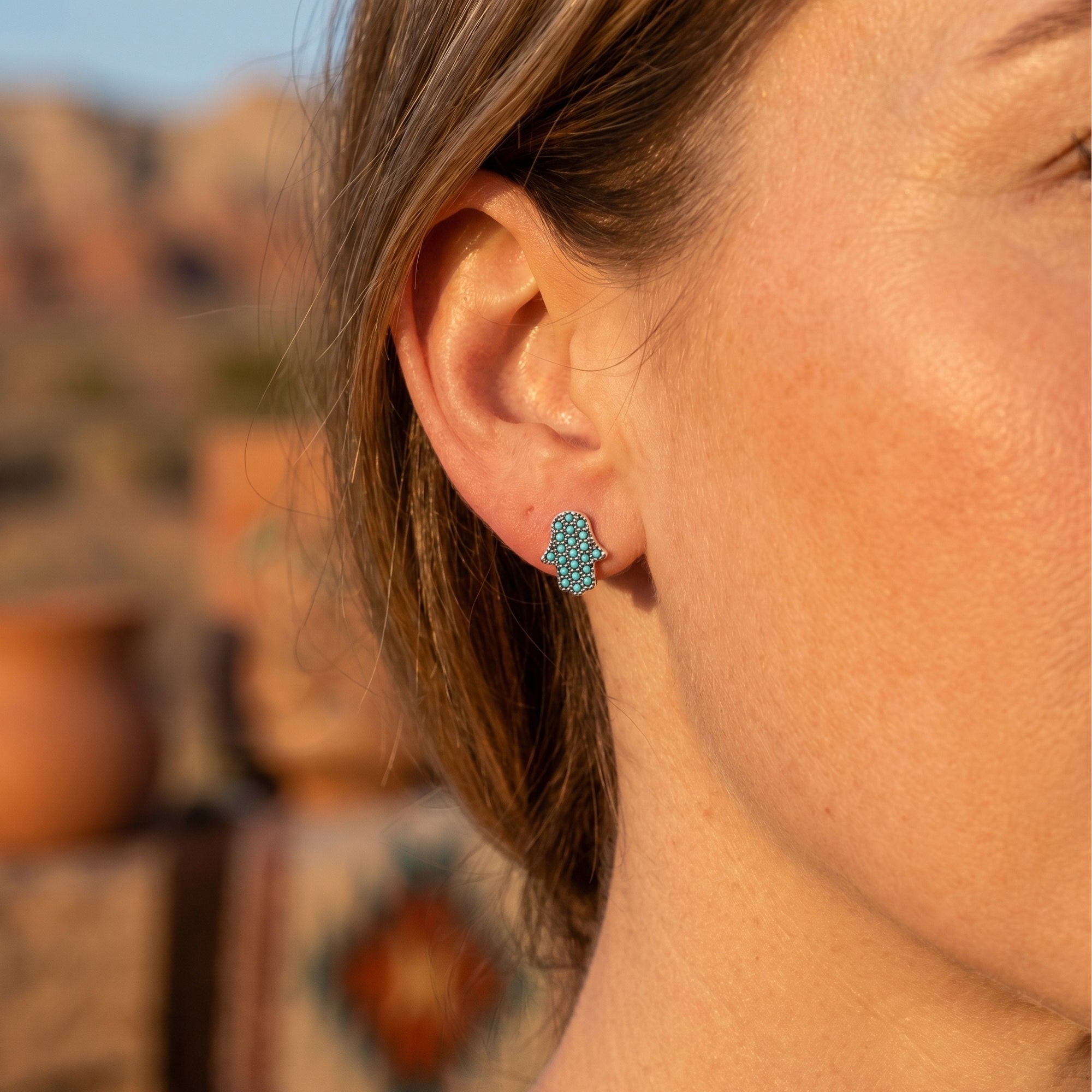 Woman wearing a silver Hamsa hand earring with turquoise stones on her earlobe.