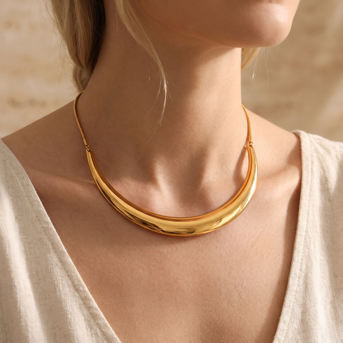 Model wearing the polished gold-tone crescent collar necklace over a white top.