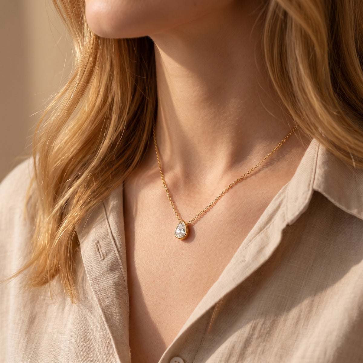 Model wearing the gold-tone teardrop bezel pendant necklace with a clear pear stone on her collarbone.