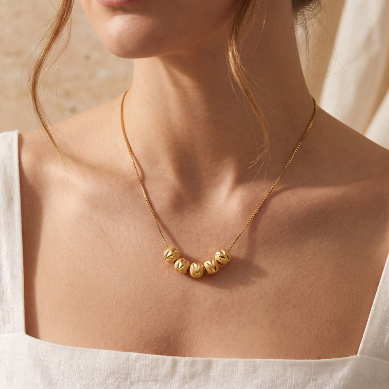 Close-up of a model wearing the gold-tone necklace with five textured beads on a fine box chain.