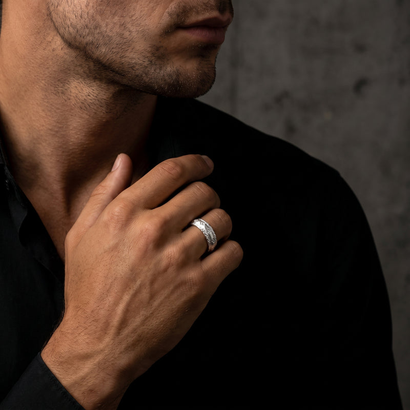 Man in a black shirt wearing the etched silver open band ring on his finger, hand raised near his chest.