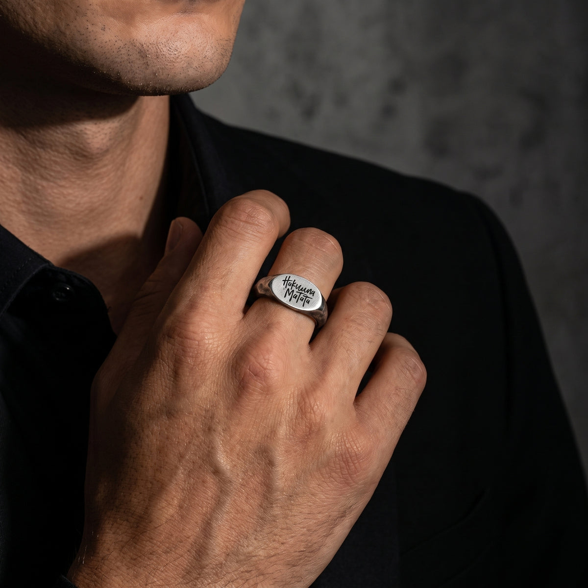 Model wearing the silver Hakuna Matata signet ring on a finger against a dark background.