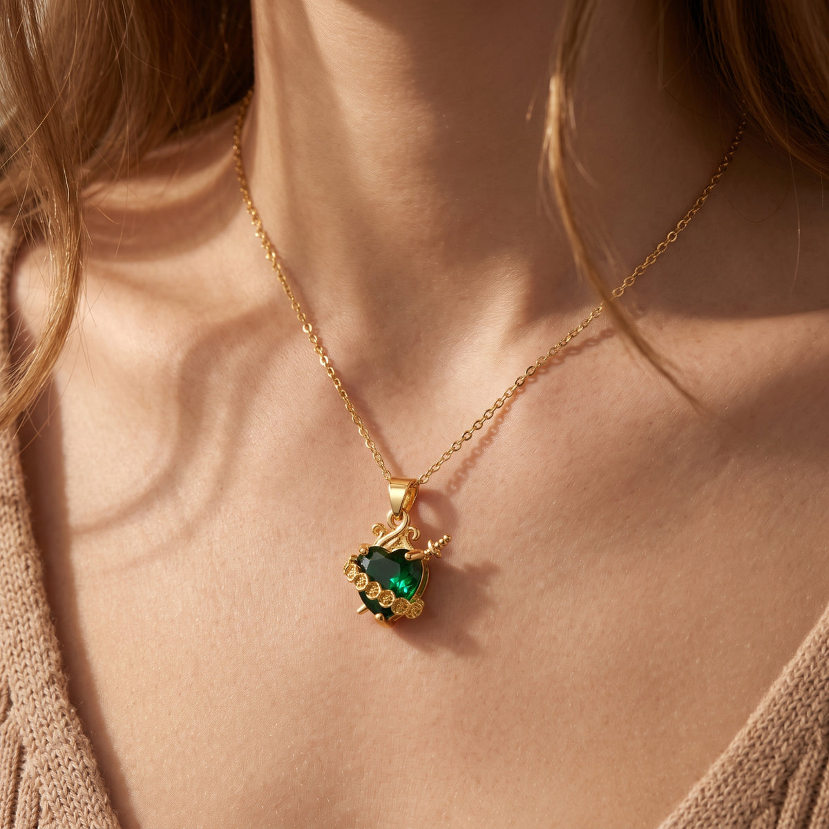 Model wearing the gold-tone necklace with a green heart and dagger pendant against her collarbone and chest.