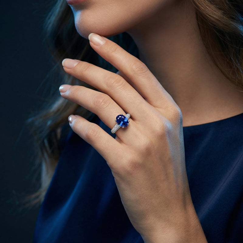 Oval tanzanite and sterling silver ring with a pave-set band, worn on a woman's hand against a dark background.