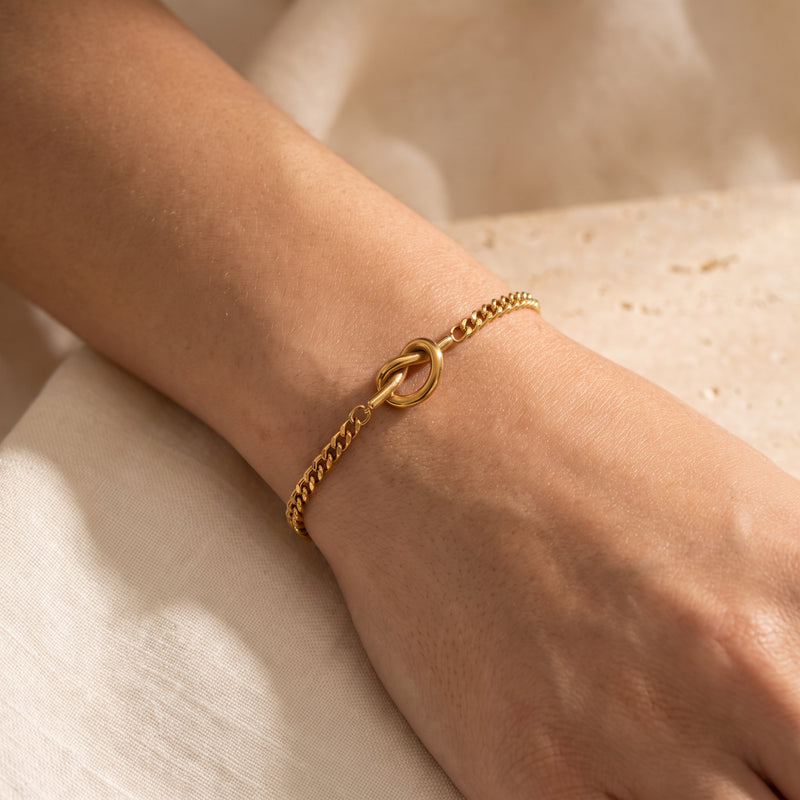 Close-up of the gold-tone knot link bracelet worn around a wrist, with the knot feature centered.
