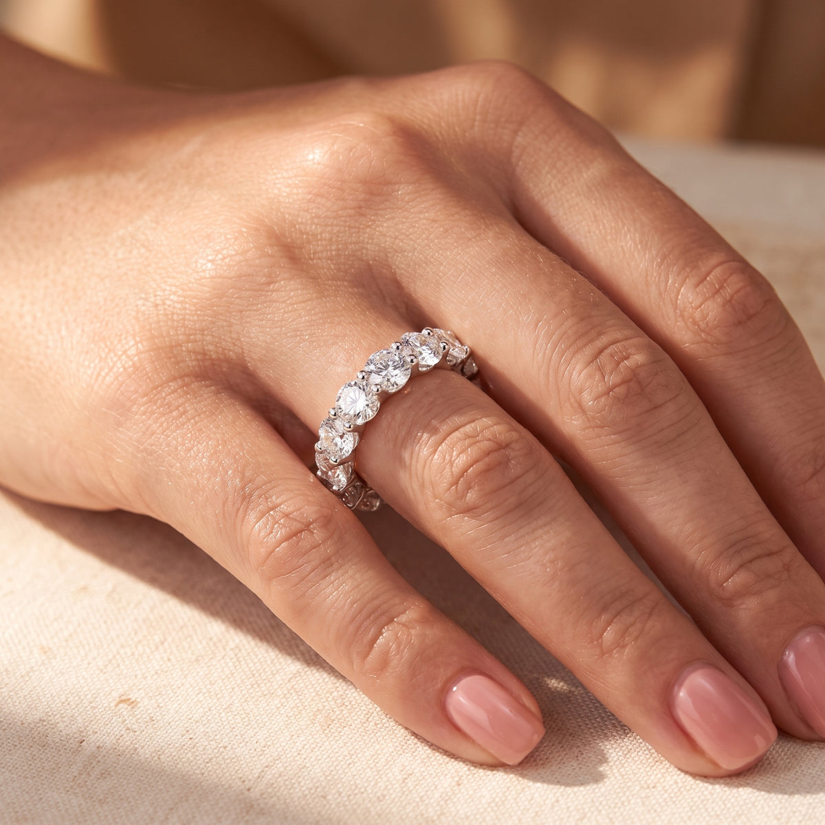 Close-up of a hand wearing a silver shared-prong eternity ring with round clear stones on the ring finger.