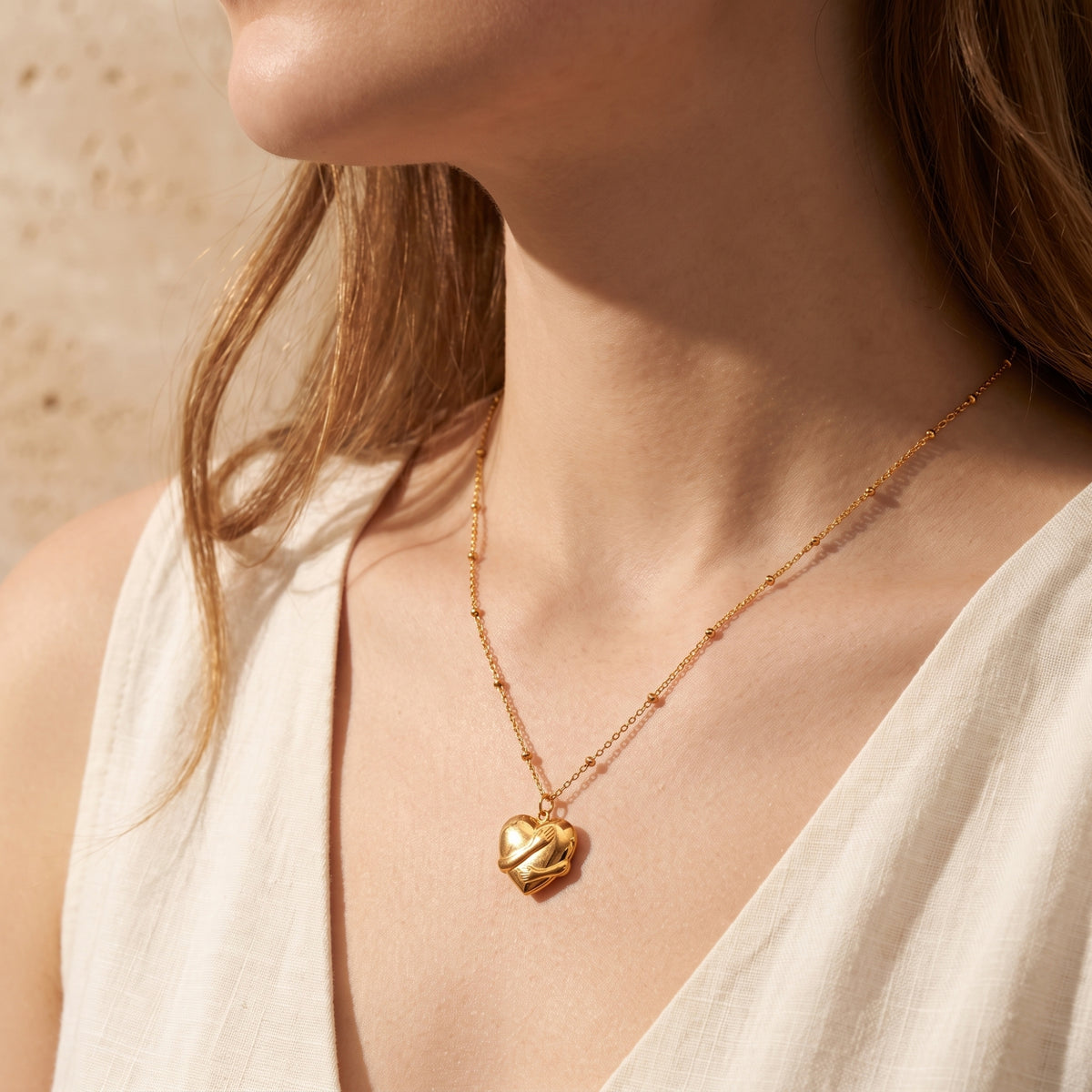 Model wearing the gold-toned hugging heart necklace, shown from neck to chest in warm sunlight.
