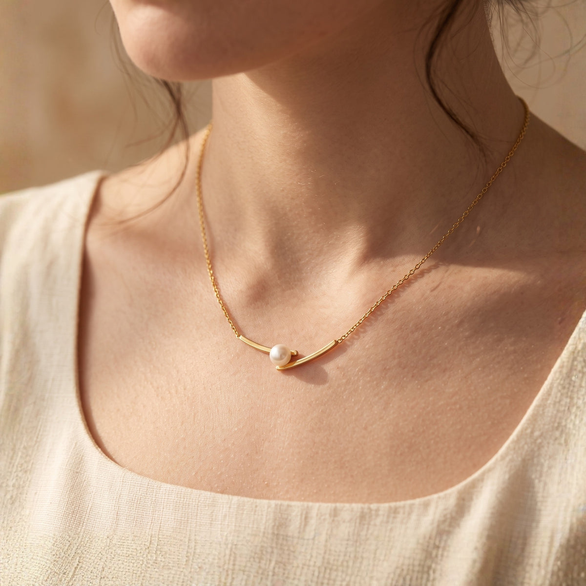 Angled close view of a model wearing the gold-tone pearl bar necklace on a cream top