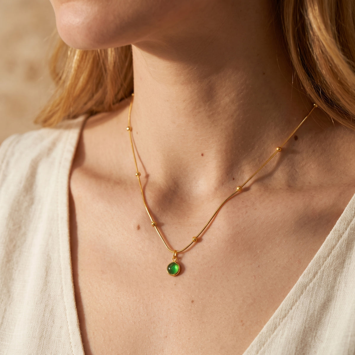 Front on-model view of a gold-tone snake chain necklace with sphere stations and green cabochon pendant.