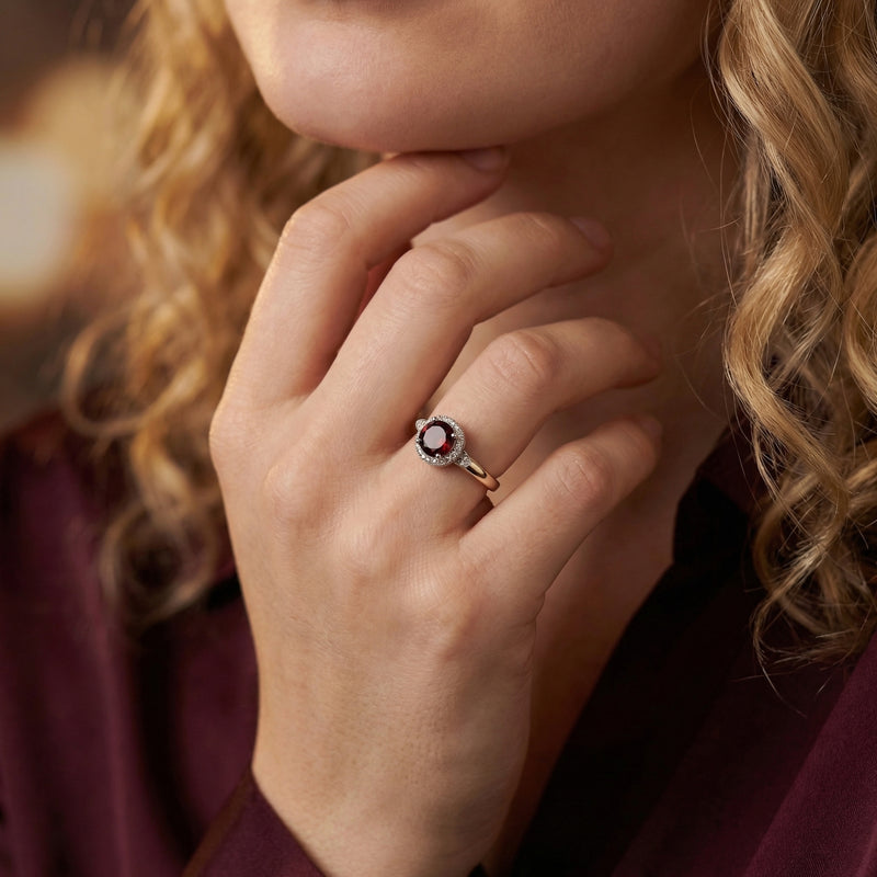 Sterling silver Alethea halo ring with a round red garnet worn on a woman's hand near her face.