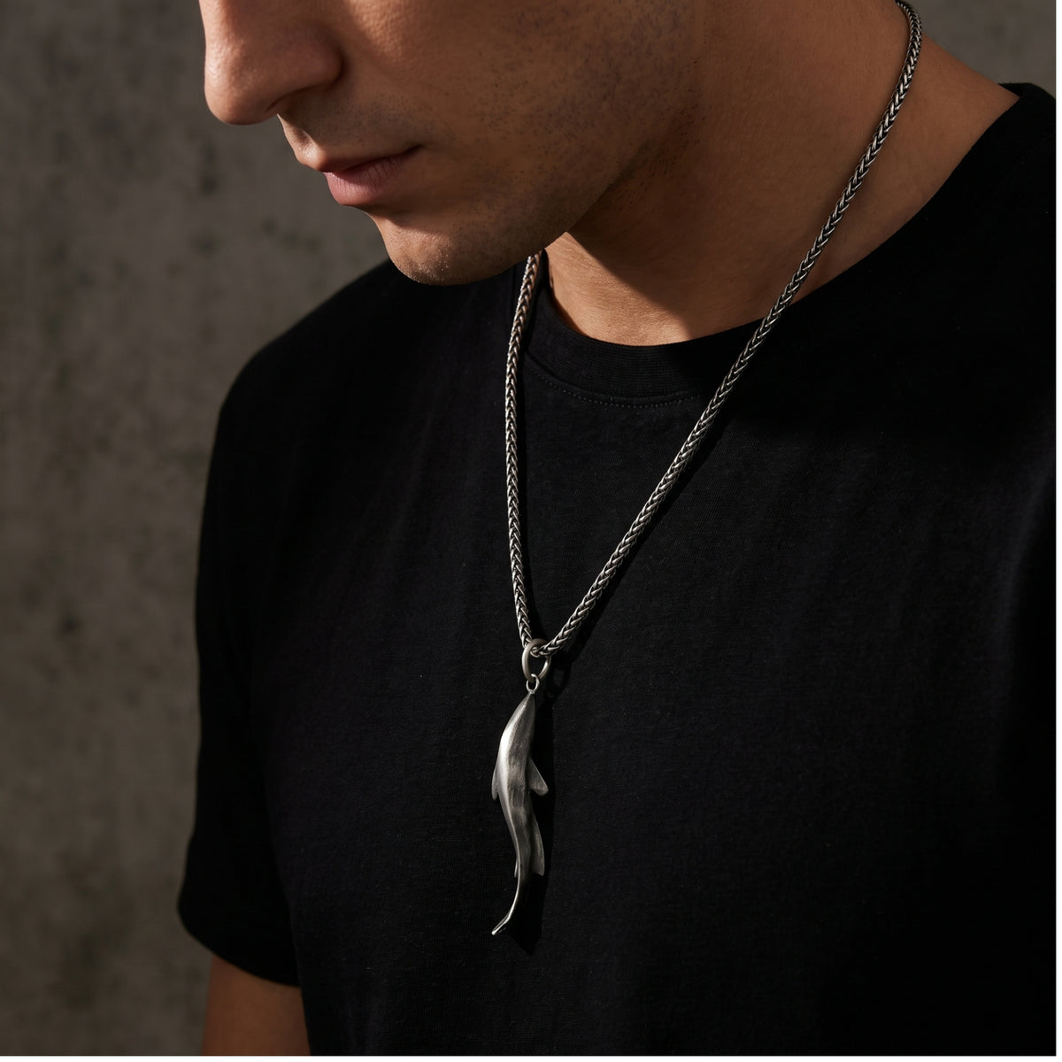 Man wearing a silver shark pendant necklace over a black T-shirt