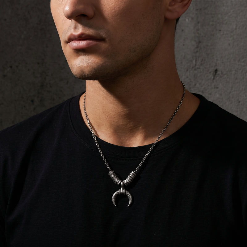 Close-up of a man wearing the crescent pendant necklace over a black shirt, with his face turned left.
