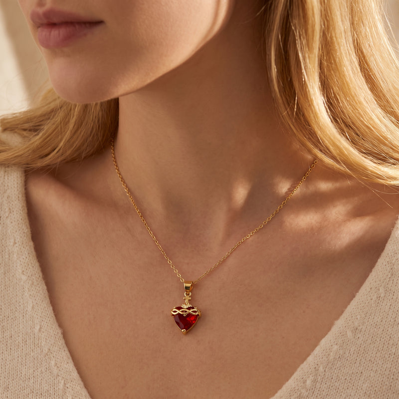 Sacred Heart necklace with a red heart crystal and gold-tone chain worn on a woman's collarbone.