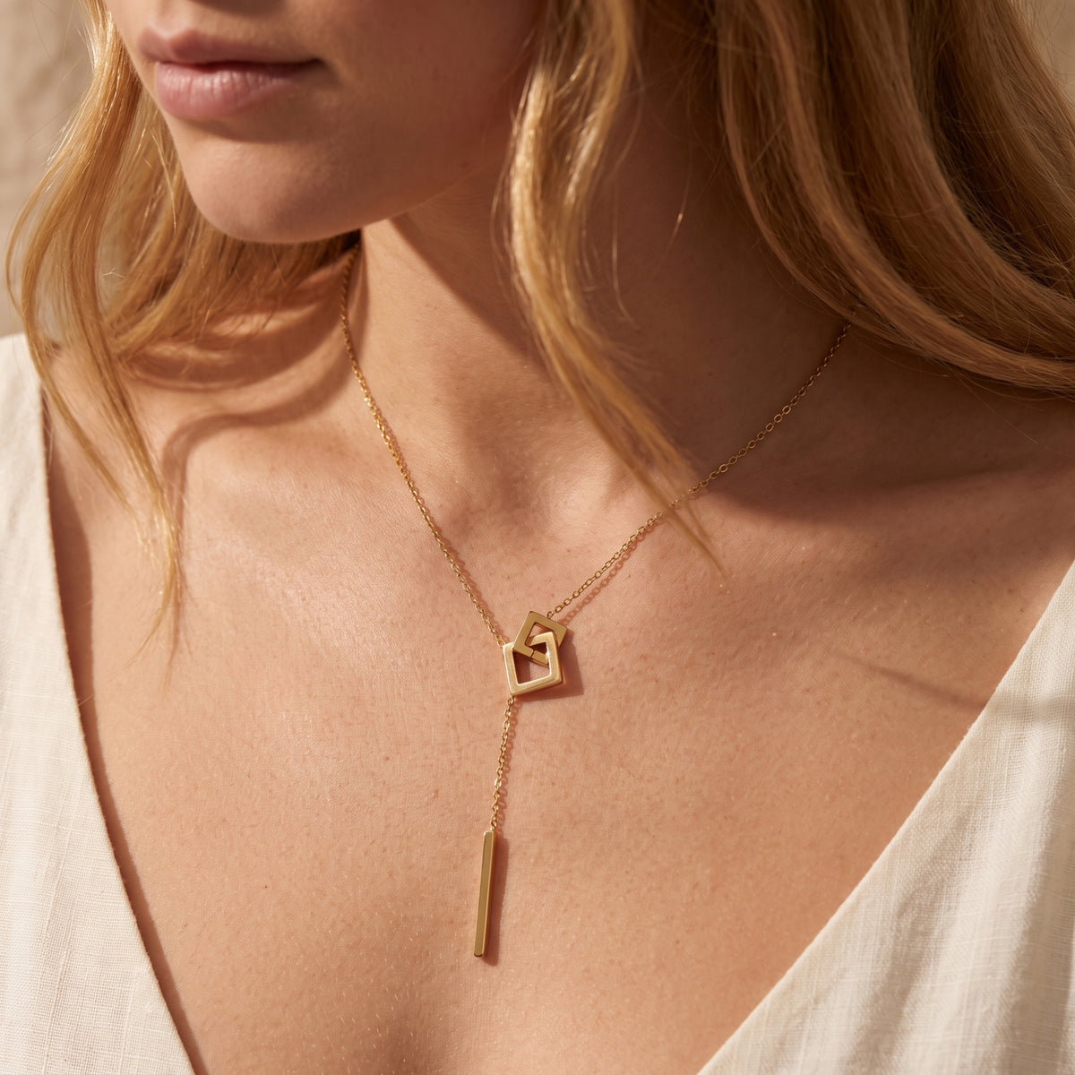 Model wearing the gold-color square link lariat necklace with a white V-neck neckline.