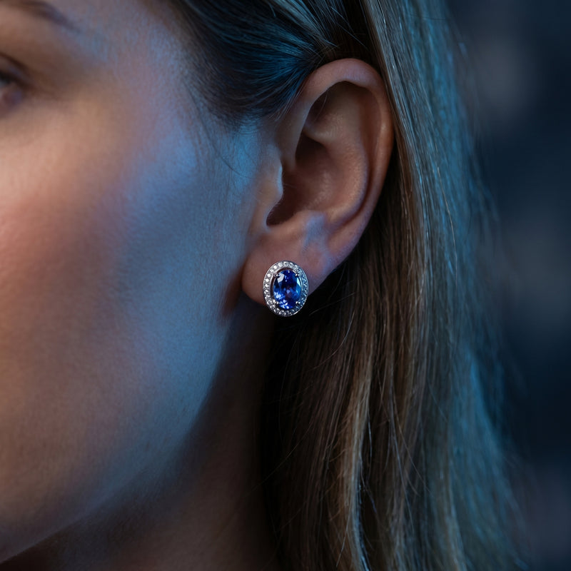 Woman wearing an oval natural tanzanite and diamond halo stud earring in 18K white gold.