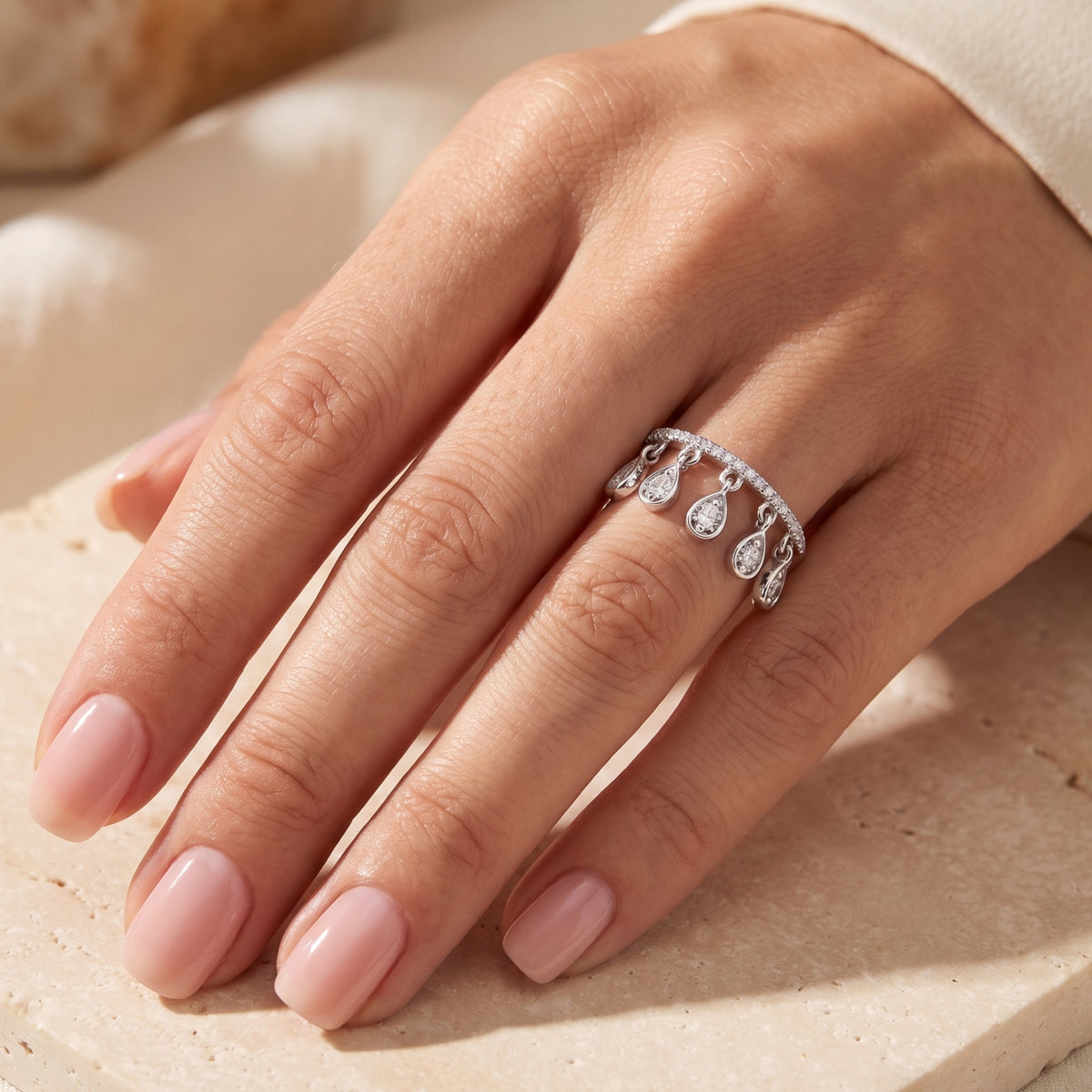 Silver ring with five dangling teardrop charms worn on a hand with pale pink manicured nails.